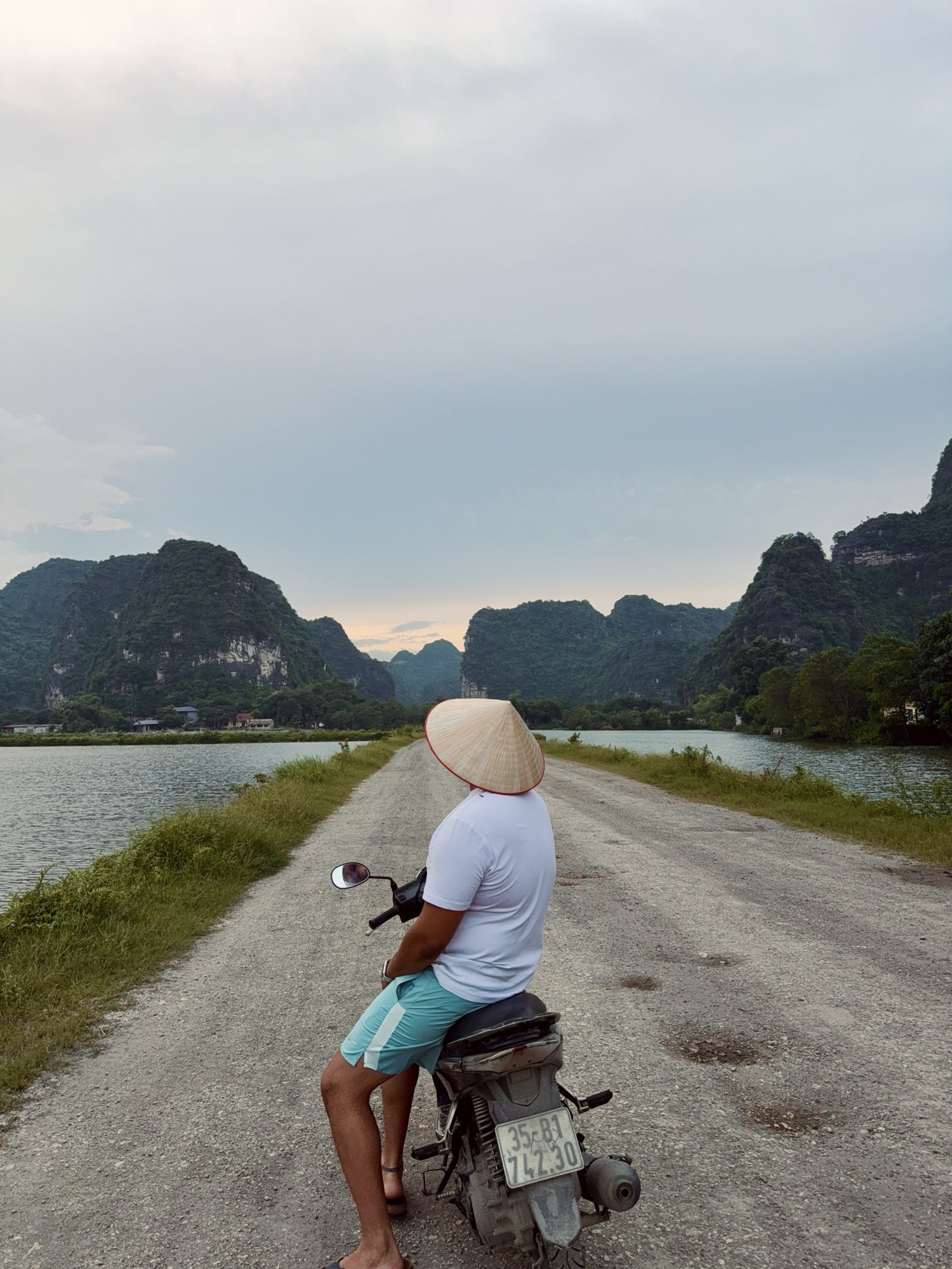 Scooter à l'arrêt sur une petite route entourée d'eau et de pics karstiques à Trang An, Ninh Binh, Vietnam