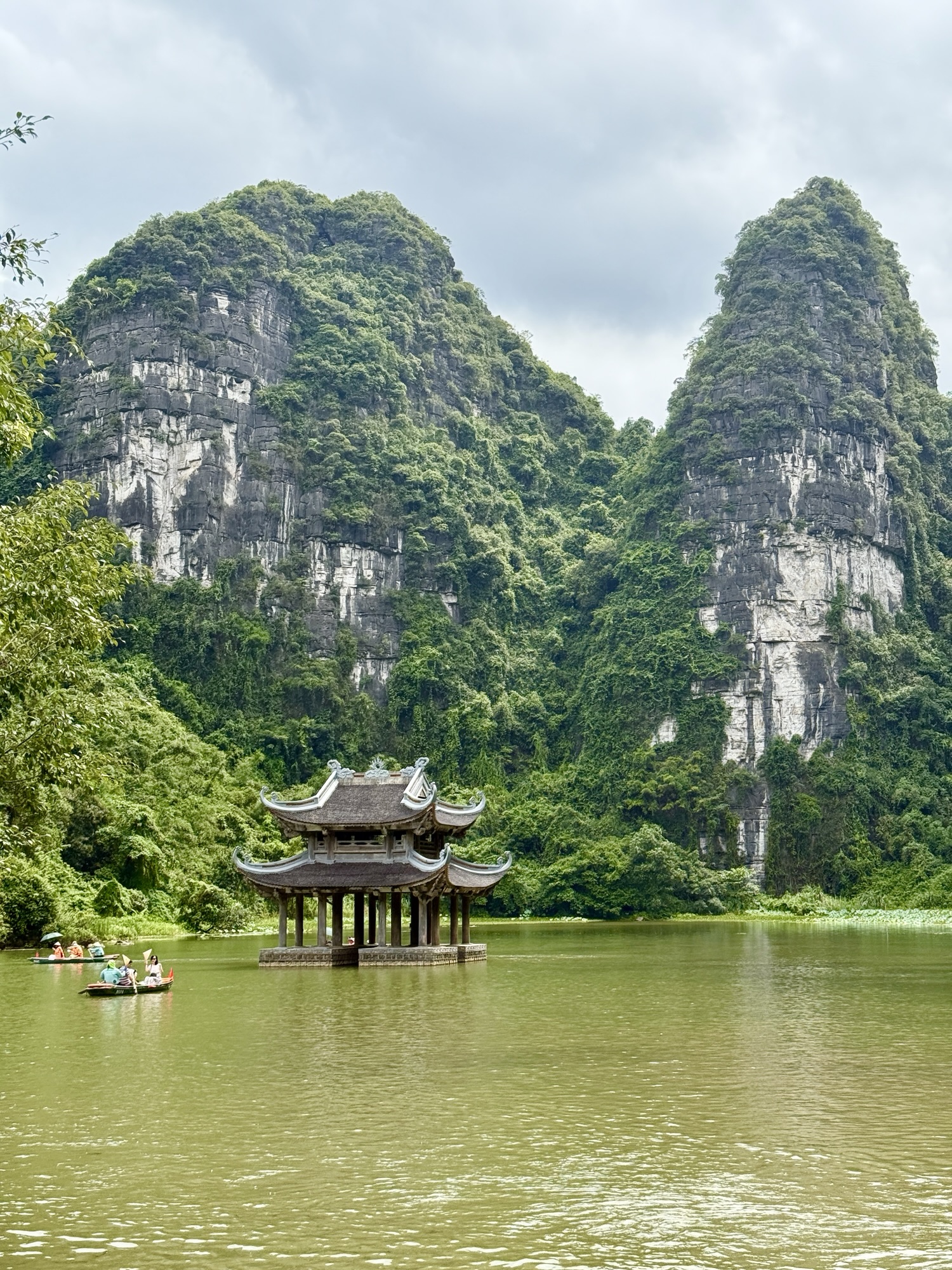 Pagode au bord de l'eau entourée de montagnes calcaires sur le site UNESCO de Trang An